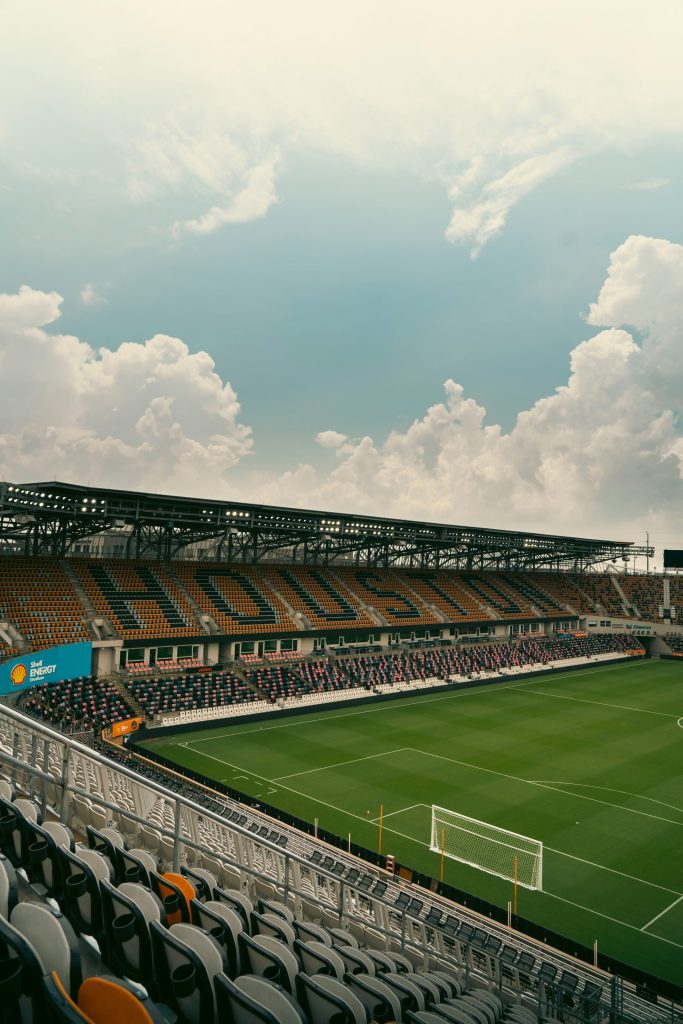 Empty soccer stadium with green field and orange seats.